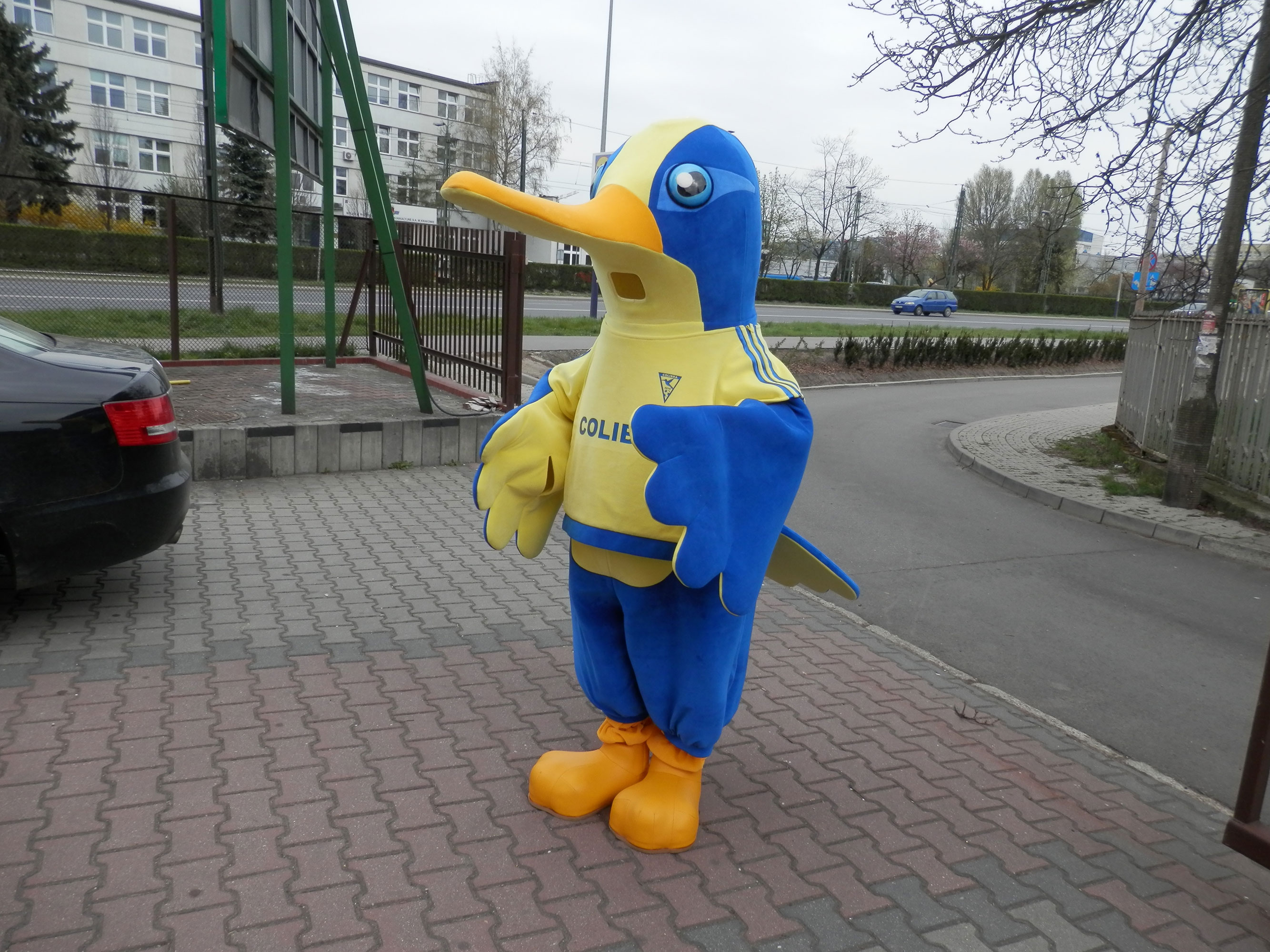 Na fotografii widnieje maskotka w postaci kolibra pozująca do zdjęcia w pobliżu siedziby firmy Elabika